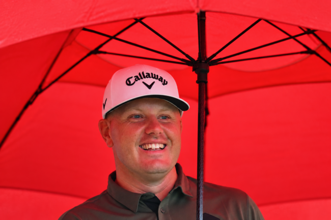 Smilende Golfspiller Under Rød Paraply